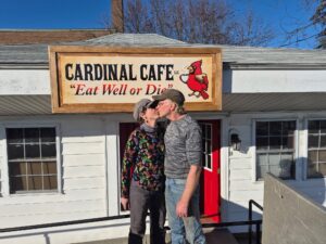 kissing in front of cardinal cafe sign